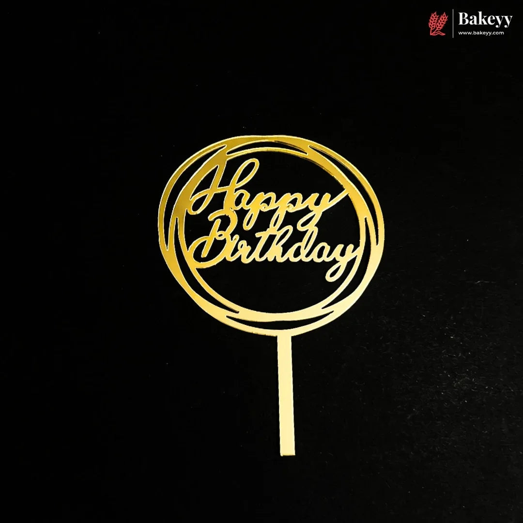 A gold metal 'Happy Birthday' cake topper with a circular cutout design and a straight stem, shown on a black background. A Bakeey brand logo is visible in the top right corner.