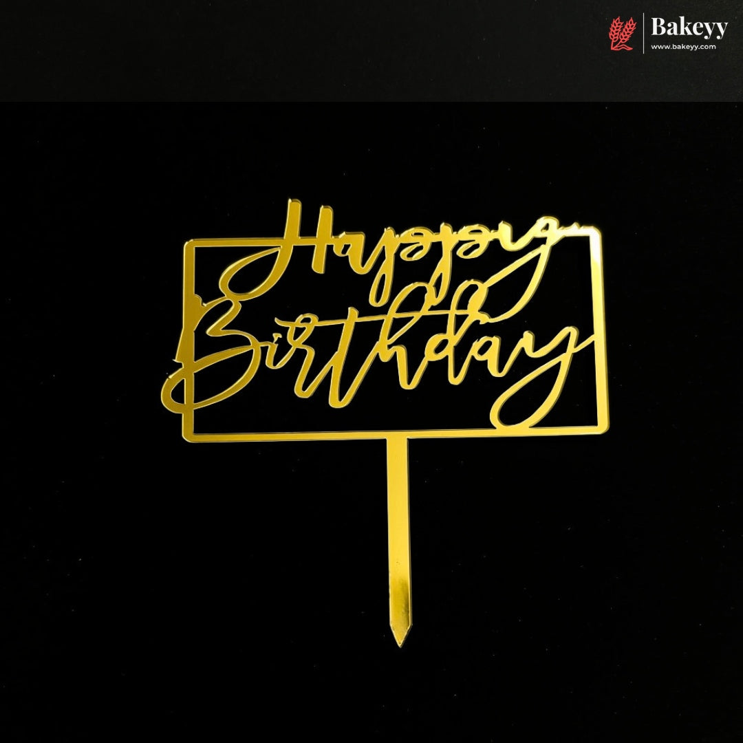 Gold metal 'Happy Birthday' cake topper with a rectangular border and stick base, shown on a black background. A Bakeey logo appears in the top right corner.