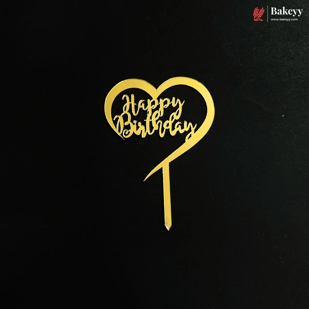 A gold heart-shaped cake topper with 'Happy Birthday' written in cursive script, displayed on a black background with a Bakeyy logo in the top right corner.