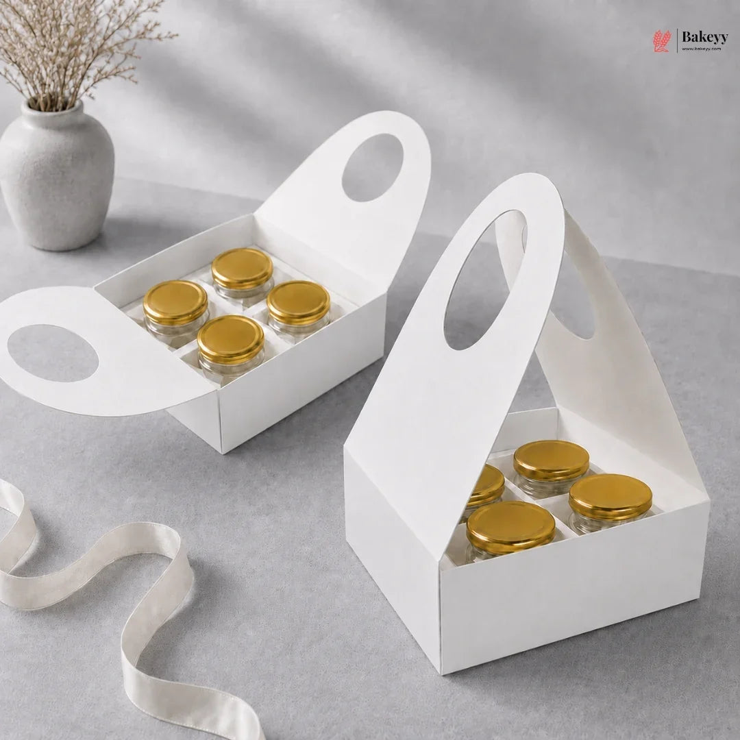 Two white gift boxes with gold lids on a gray surface, featuring a ribbon and a vase in the background.