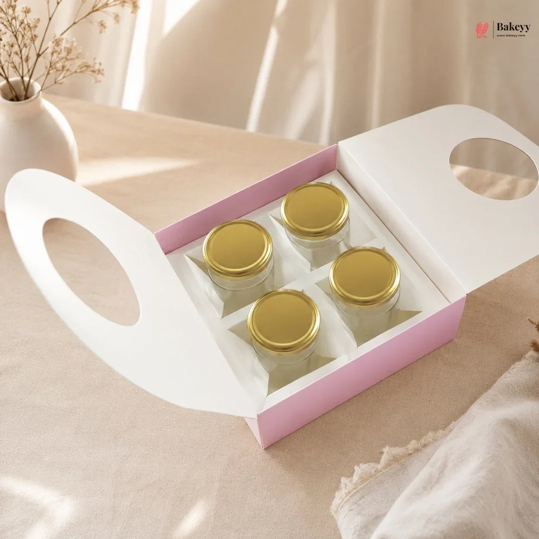 Set of small jars with gold lids in a pink and white box on a light surface.