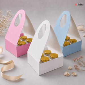 Three small cardboard boxes with gold lids, one pink, one white, and one blue, on a light gray background.