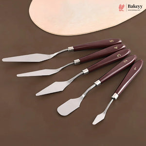 Four pastry spatulas with dark reddish-brown wooden handles and silver stainless steel blades, arranged diagonally on a brown surface with a wooden paddle partially visible in the background. The Bakeey logo is in the top right corner.