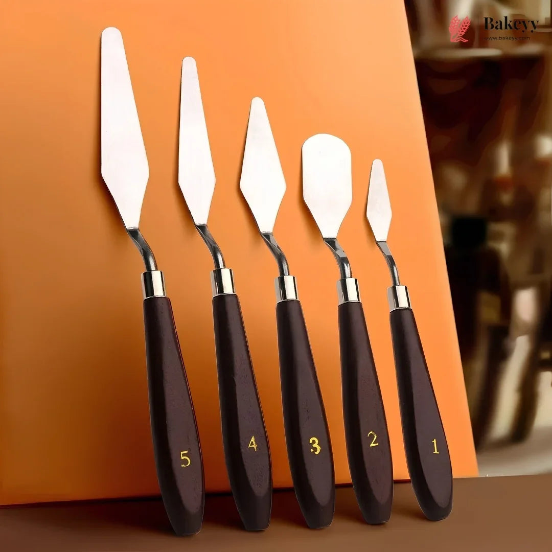 Five metal cake and pastry spatulas with dark brown wooden handles numbered 1 to 5 in gold, arranged in descending size order against a warm orange background.