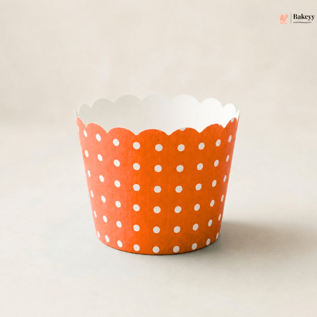 An orange paper cupcake liner with a white polka dot pattern and scalloped edge, photographed on a neutral light beige background.