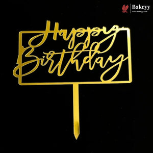 Gold metal 'Happy Birthday' cake topper with a rectangular frame and stick, shown on a black background. A Bakeey logo is visible in the top right corner.