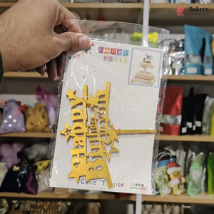 Hand holding a package of 'Happy Birthday' cake topper with a blurred store shelf in the background.