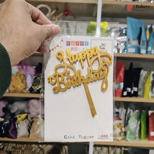 Gold 'Happy Birthday' cake topper in packaging held by a hand with a store shelf in the background.