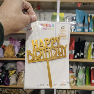 Hand holding a 'Happy Birthday' cake topper packaging in a store setting.
