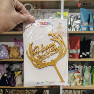Gold 'Happy Birthday' cake topper with antlers on a clear packaging against a store shelf background.