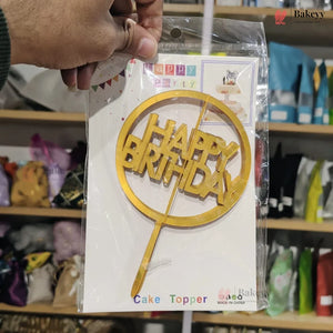 Gold 'Happy Birthday' cake topper in packaging held by a hand with a store shelf in the background.