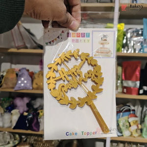Gold cake topper with decorative elements in a clear package, held by a hand in a store setting.