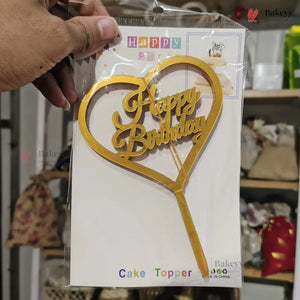 Gold 'Happy Birthday' cake topper in packaging held by a hand.