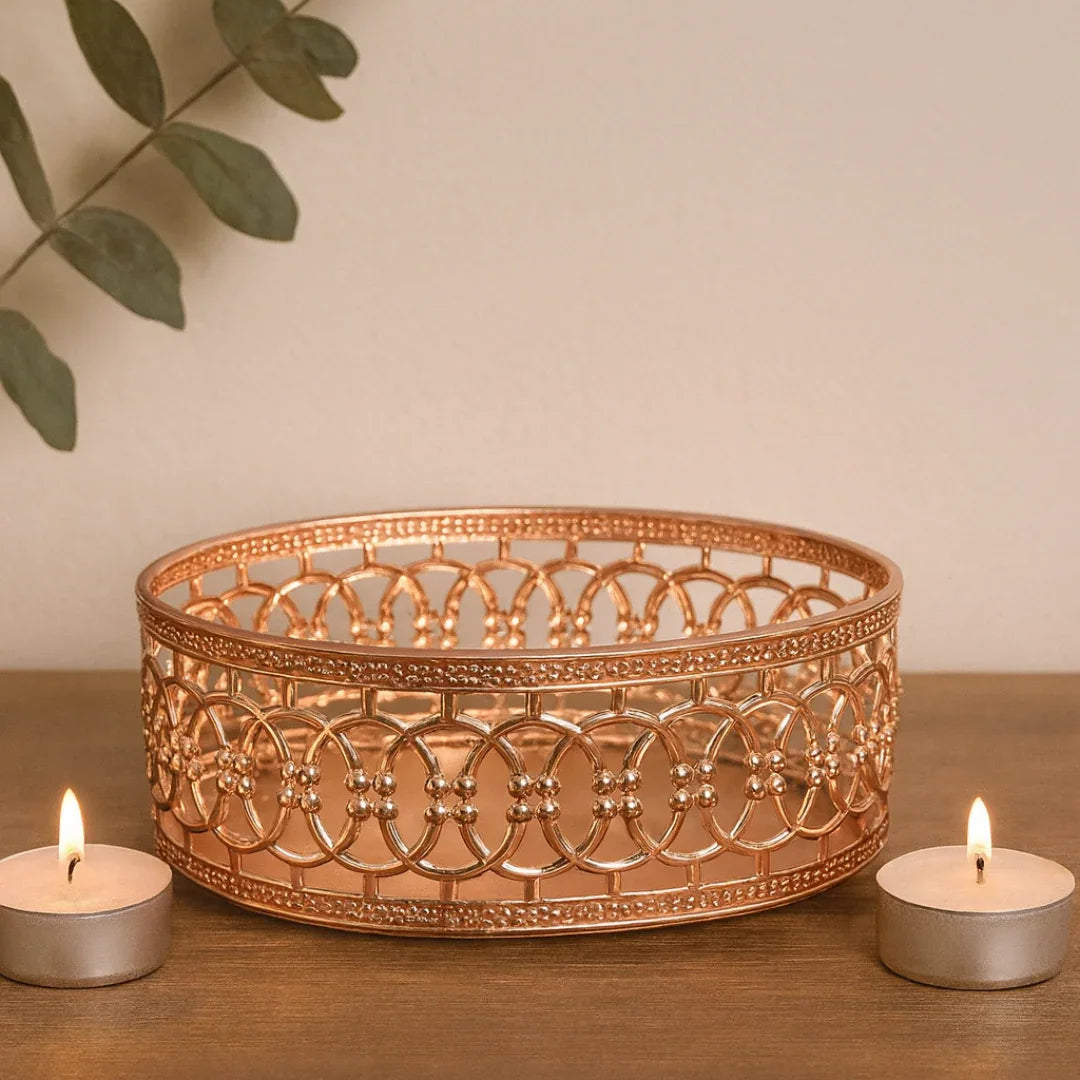Decorative copper bowl with two lit tealights on a wooden surface.