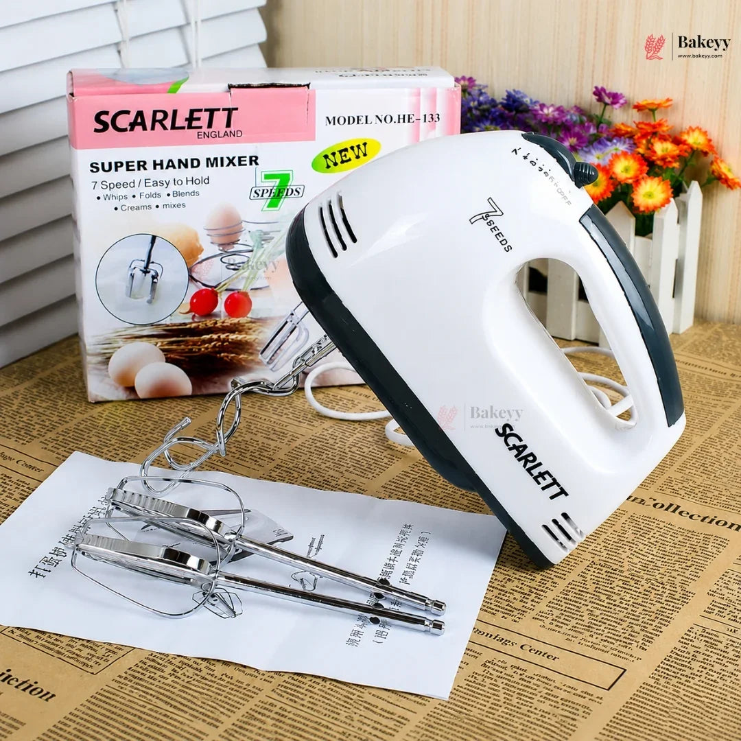 Scarlett hand mixer with attachments on a newspaper, next to its packaging and flowers in the background.