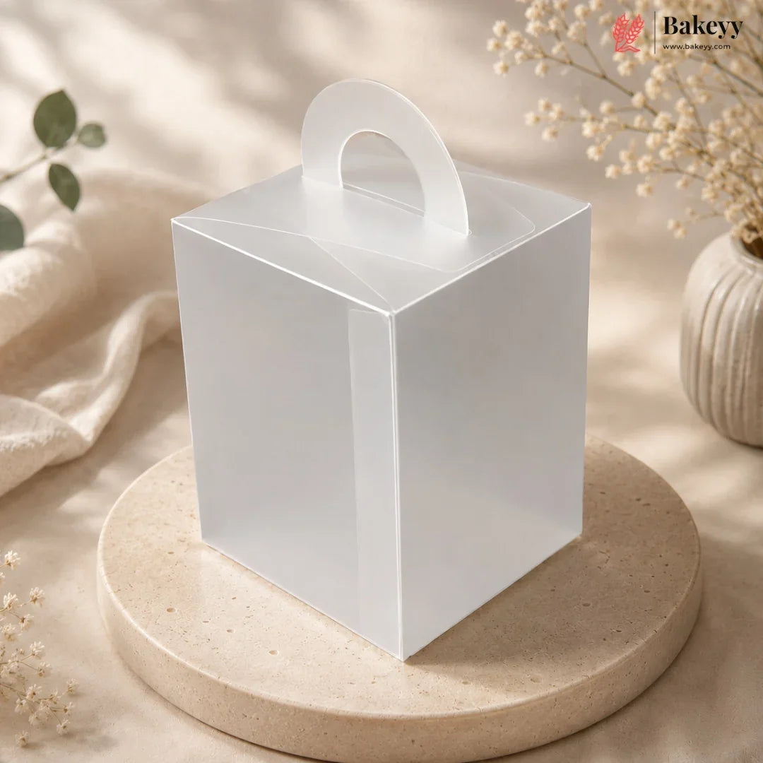 White square gift box with a handle on a beige surface with decorative elements.