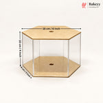 A hexagonal clear acrylic display box with tan cardboard-like base and top panels, shown on a white background with overlaid dimensions: 16 cm / 6 inch across the top, 10 cm / 4 inch height, and 8 cm / 3 inch depth. Bakeyy logo appears in the top right.