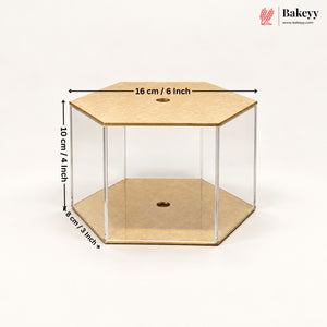 A hexagonal clear acrylic display box with tan cardboard-like base and top panels, shown on a white background with overlaid dimensions: 16 cm / 6 inch across the top, 10 cm / 4 inch height, and 8 cm / 3 inch depth. Bakeyy logo appears in the top right.