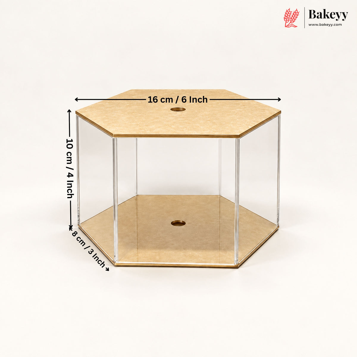 A hexagonal clear acrylic display box with tan cardboard-like base and top panels, shown on a white background with overlaid dimensions: 16 cm / 6 inch across the top, 10 cm / 4 inch height, and 8 cm / 3 inch depth. Bakeyy logo appears in the top right.