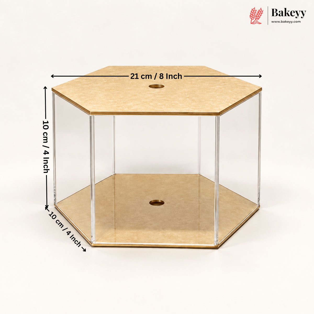 Hexagonal acrylic display case with a light wood top and bottom, shown with dimension lines indicating 21 cm / 8 inch across the top, 10 cm / 4 inch height, and 10 cm / 4 inch depth. The Bakeyy logo is visible in the top right corner.