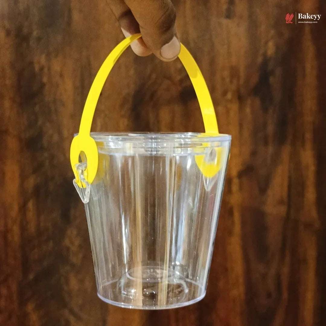 Clear plastic bucket with yellow handle held by a hand against a wooden background