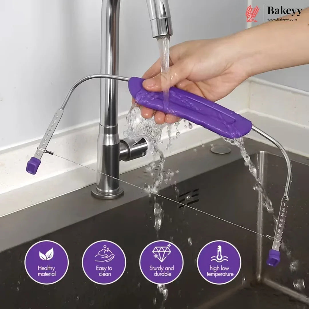 A hand holds a purple silicone kitchen tool over a running faucet in a stainless steel sink. The tool has curved metal arms with purple end caps and is shown under running water.