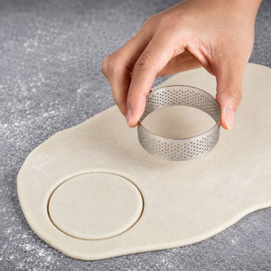 Hand using a metal cookie cutter on a piece of dough on a gray surface