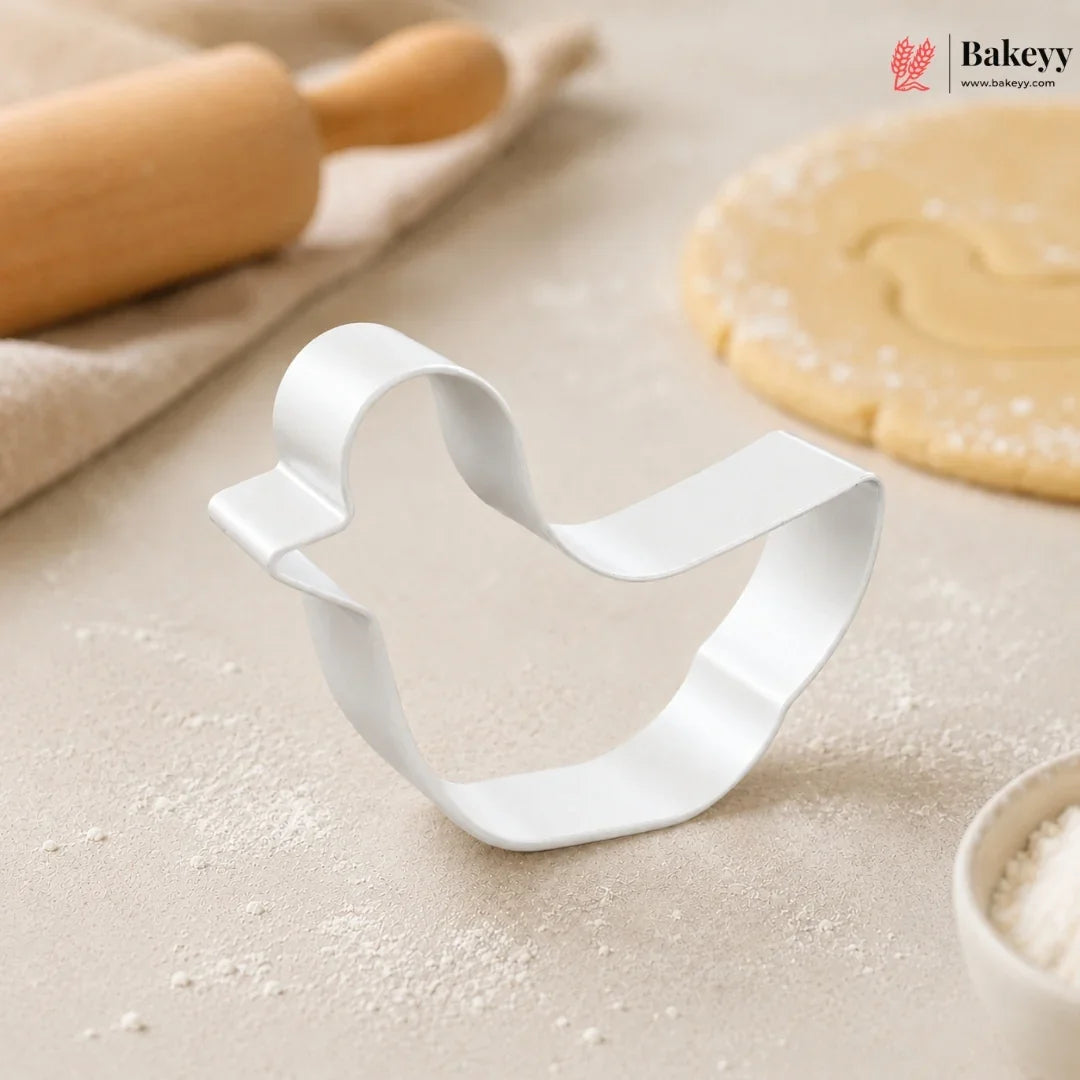 Metallic bell-shaped cookie cutter on a baking surface with a rolling pin and dough in the background, featuring the Bakey brand.
