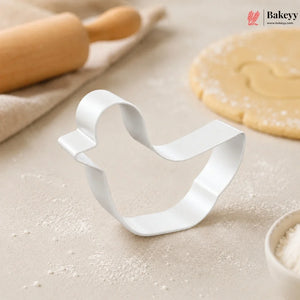 Metallic bell-shaped cookie cutter on a baking surface with a rolling pin and dough in the background, featuring the Bakey brand.