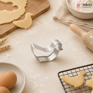 Bakey bird-shaped cookie cutter on a baking surface with cookies and utensils.