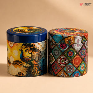 Two decorative cylindrical metal tins with colorful printed designs, one featuring a peacock and traditional landscape, and the other with a geometric mandala pattern, set against a warm beige background.