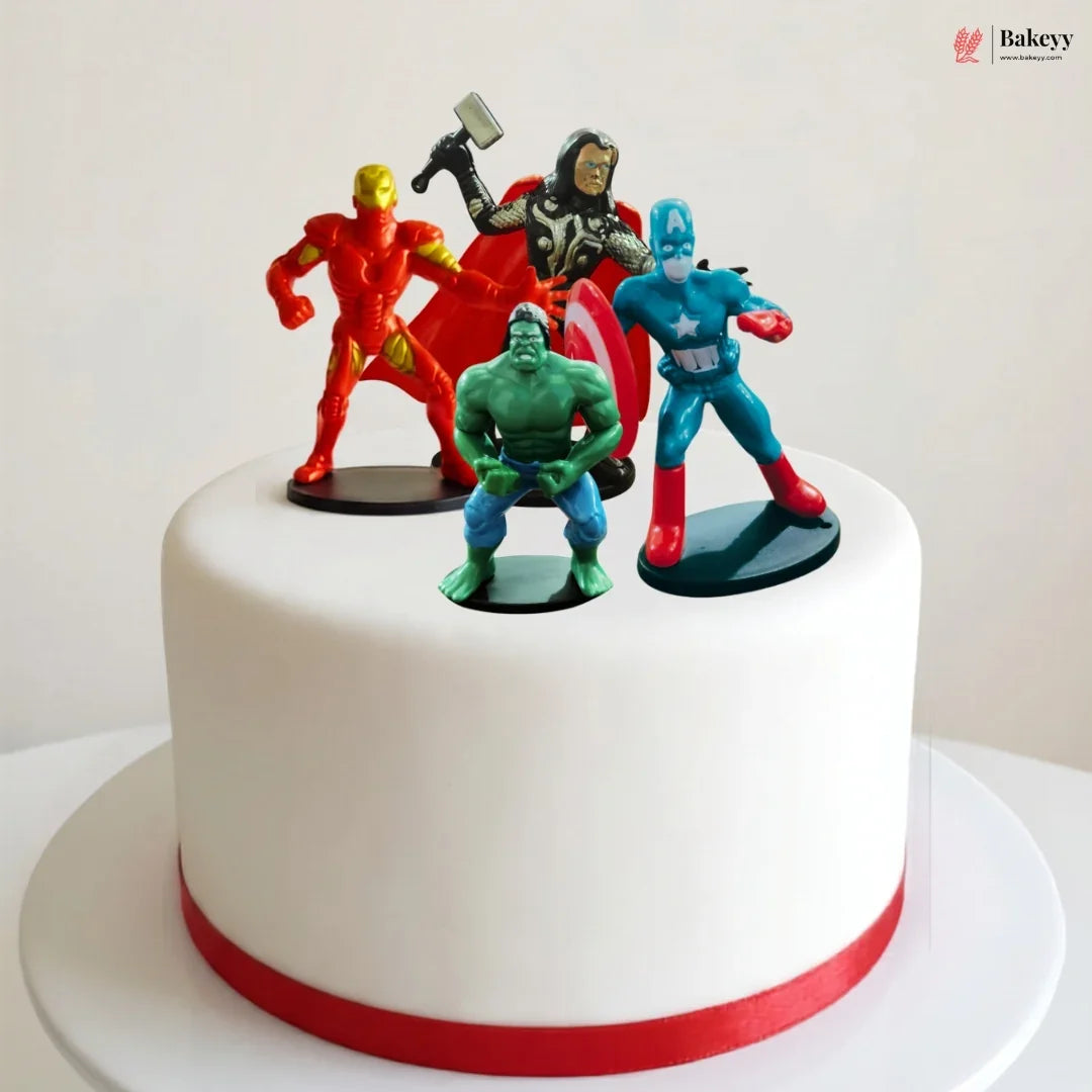 White cake with superhero figurines on top, featuring characters like Iron Man, Captain America, and Hulk.
