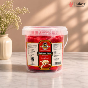 Bucket of red sugar paste with a label on a light surface, featuring the Bakeyy brand.