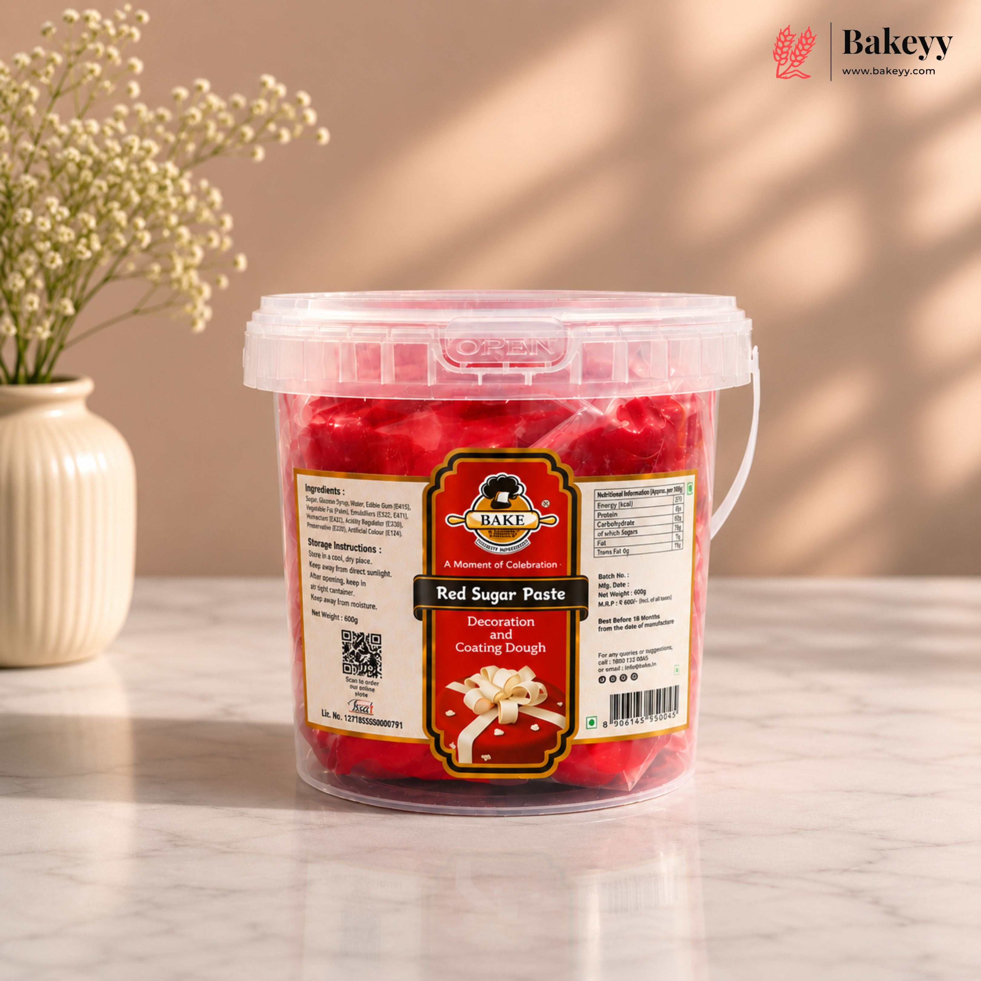Bucket of red sugar paste with a label on a light surface, featuring the Bakeyy brand.