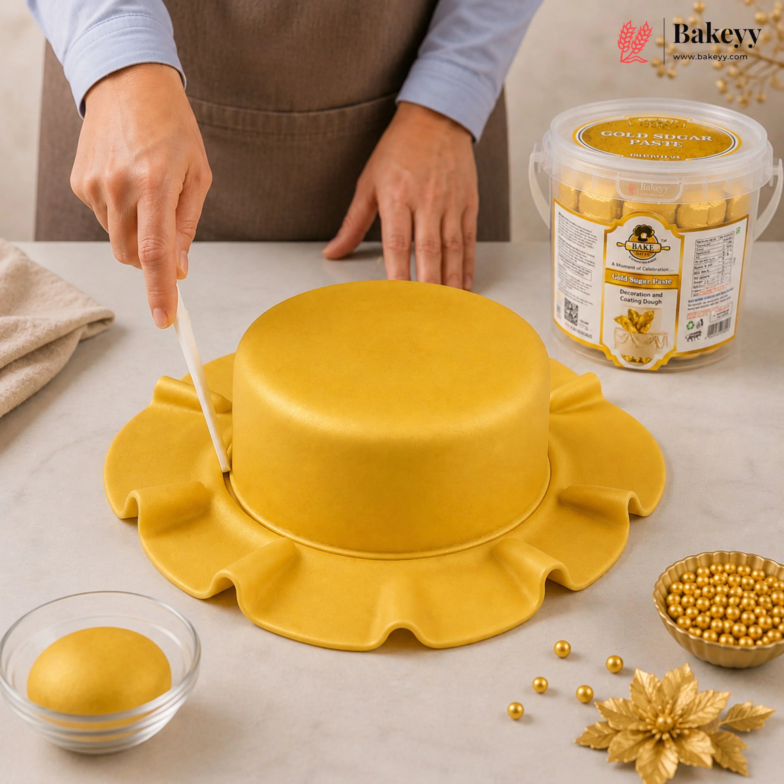 Person decorating a yellow cake with gold decorations on a table, featuring Bakey packaging.