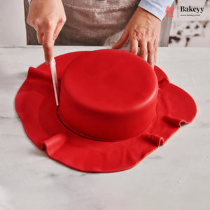 Person cutting a red cake with a knife on a white surface, with 'Bakeyy' branding visible.