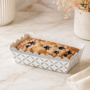 Loaf of bread in a decorative paper container on a marble surface with 'Bakey' branding.