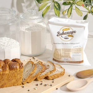 Bag of Bakescape flour with sliced bread and baking ingredients on a table