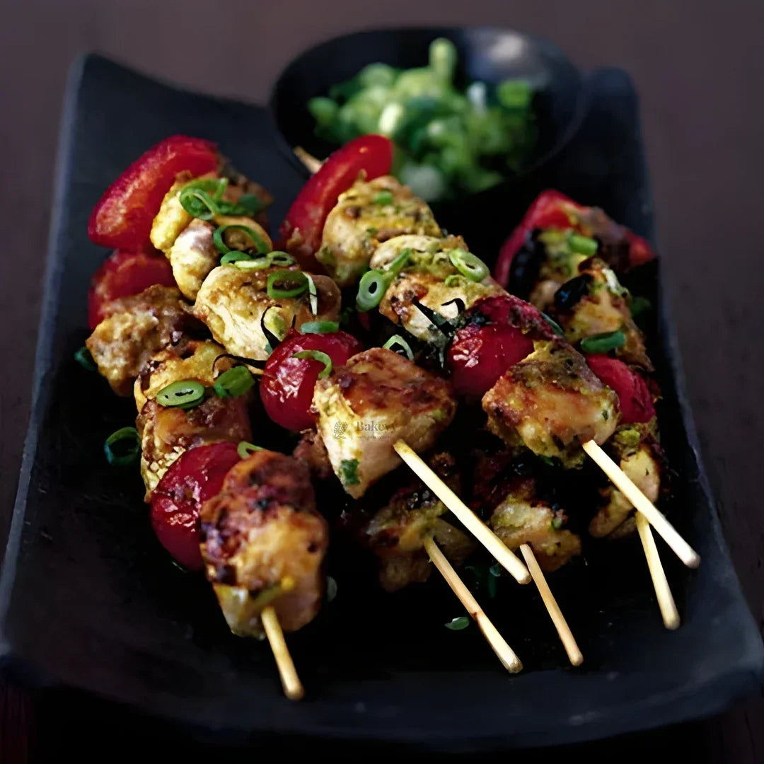 Grilled chicken and tomato skewers on bamboo sticks, garnished with spring onions on a black platter