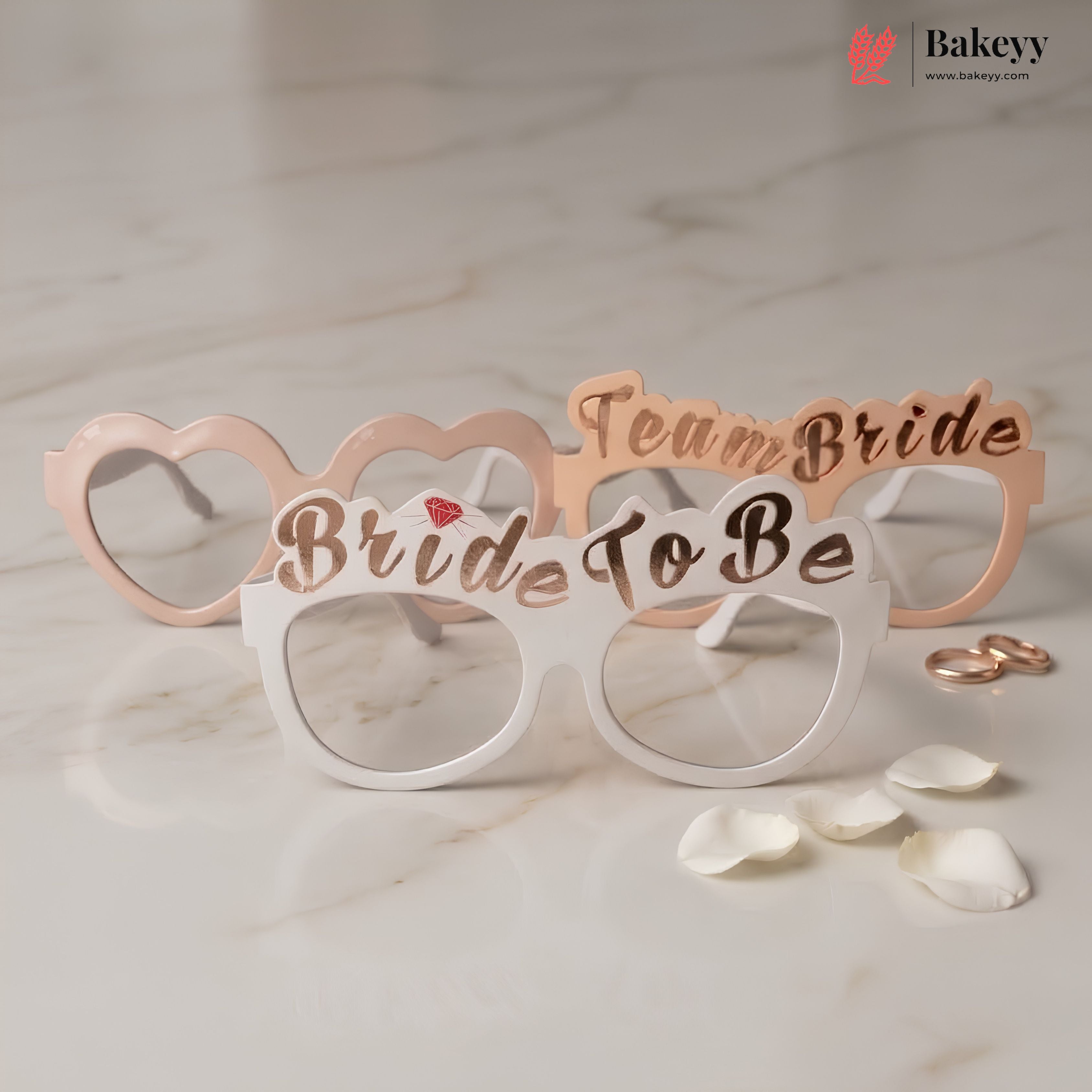Bride to be glasses with 'Team Bride' text on a marble surface with rose gold rings and petals.