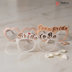 Bride to be glasses with 'Team Bride' text on a marble surface with rose gold rings and petals.
