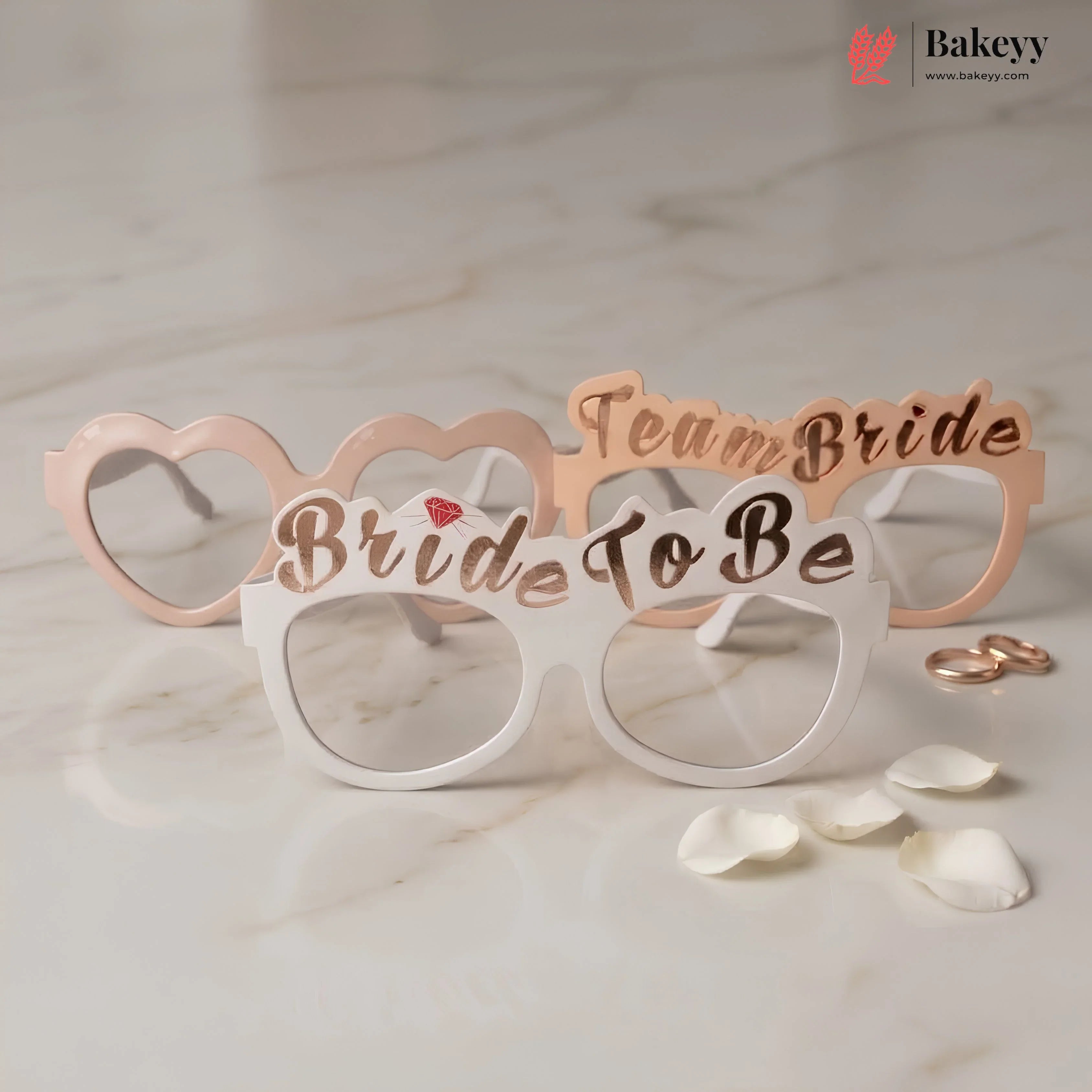 Bride to be glasses with 'Team Bride' text on a marble surface with rose gold rings and petals.