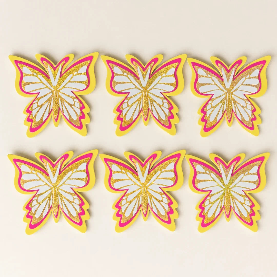 Set of six butterfly-shaped decorations with pink, yellow, and white colors on a beige background.