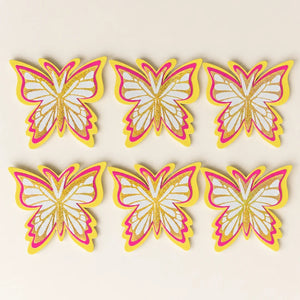 Set of six butterfly-shaped decorations with pink, yellow, and white colors on a beige background.
