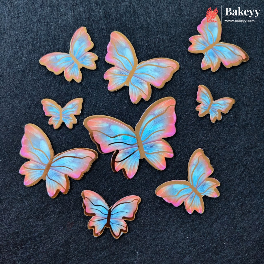 Seven butterfly-shaped sugar cookies with iridescent pastel wings in shades of blue, pink, and purple, arranged on a dark textured background. The Bakeyy logo is visible in the top right corner.
