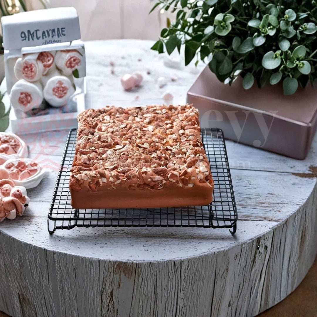 Square nut-topped cake on cooling rack, baking supplies in background, Bakeyy baking products