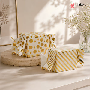 Two boxes wrapped in gold and white patterned paper on a light surface with a blurred indoor background.