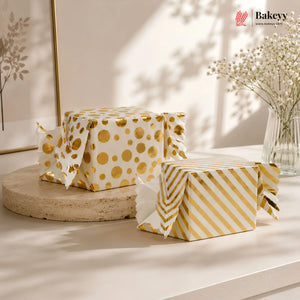 Two boxes wrapped in gold and white patterned paper on a light surface with a blurred indoor background.