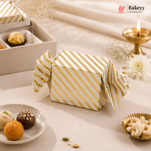 Gold and white striped gift box on a decorative table with snacks and a candle.