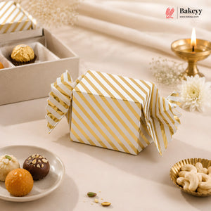 Gold and white striped gift box on a decorative table with snacks and a candle.